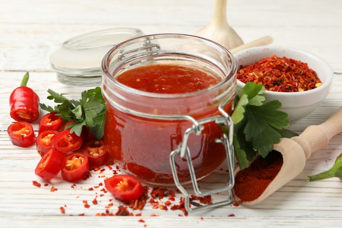 Composition with red hot sauce and ingredients on wooden background