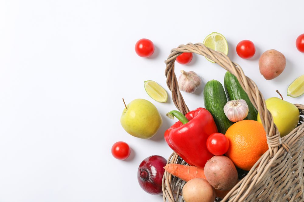 Wicker basket, vegetables and fruits on background, space for text