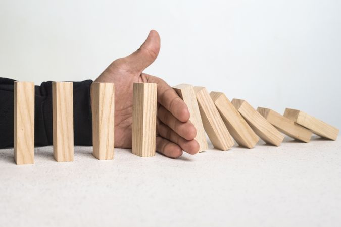 male hand stop falling wooden blocks. domino effect or risk protection strategy concept