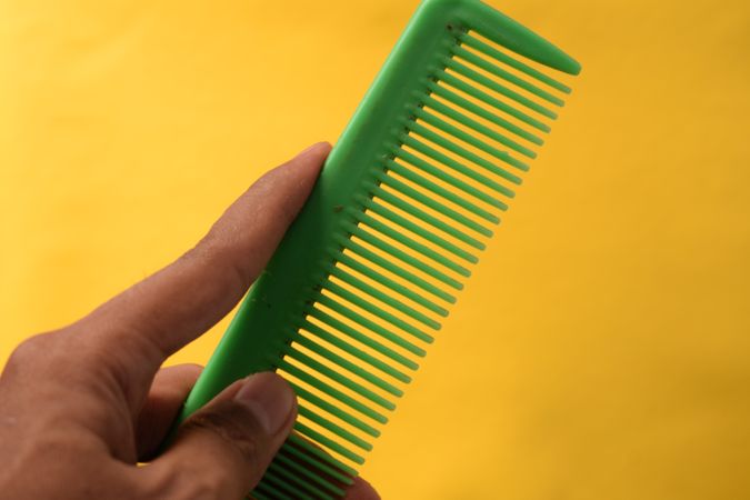 Hand holding green hair comb diagonally against yellow background