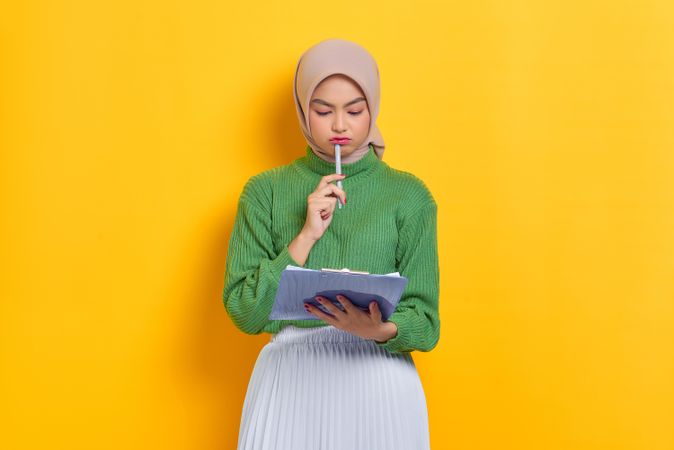 Woman in headscarf looking down at clipboard with pen