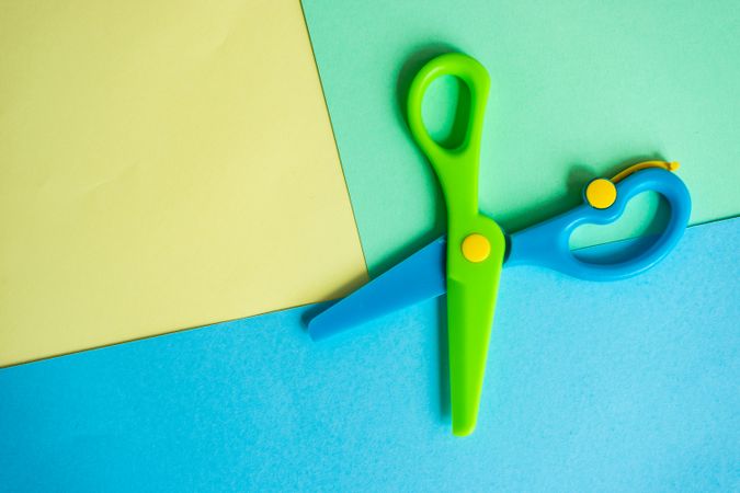Open blue & green safety scissors on paper background