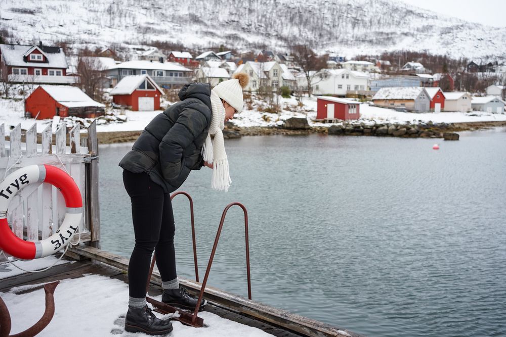 Woman on waterfront against small town at snowy foothill