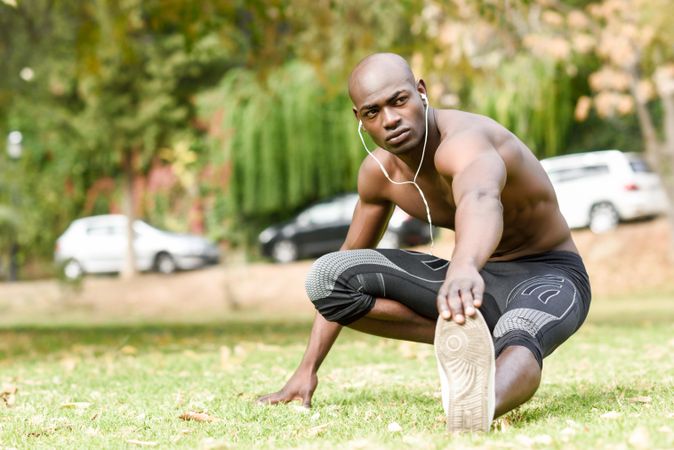 Male stretching legs with shirt off listening to music on headphones