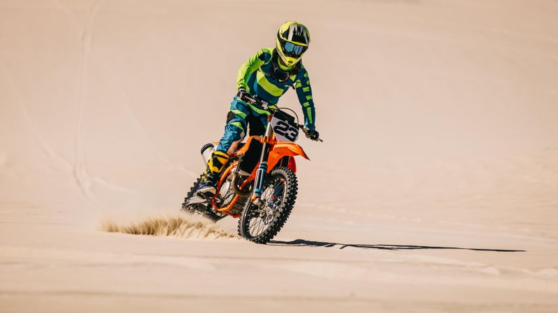 Moto racer riding upright over sand in desert