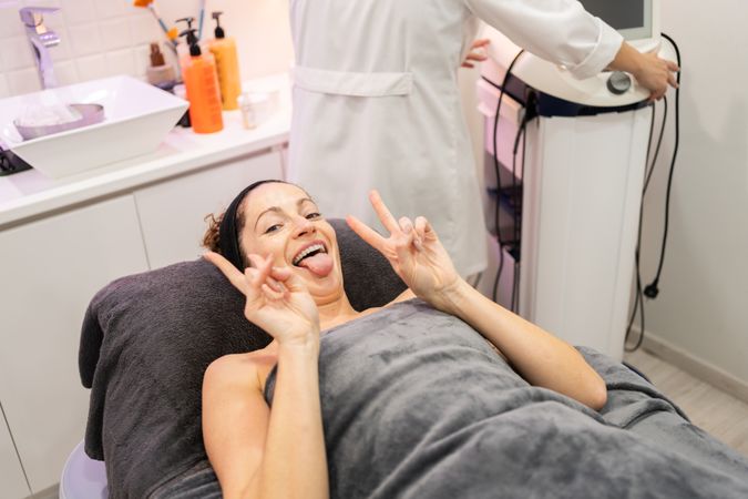 Happy woman making funny face and showing V sign before beauty treatment