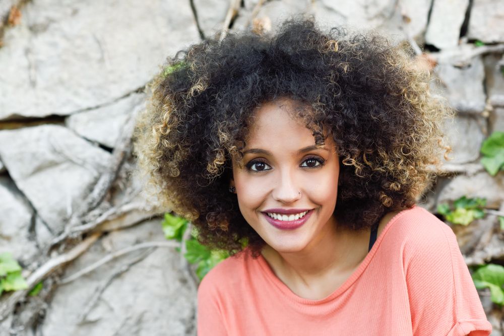 Portrait of smiling Black woman with afro hairstyle in front of stone wall