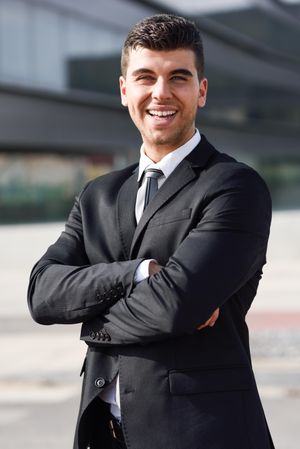 Smiling man in suit standing outside with arms crossed
