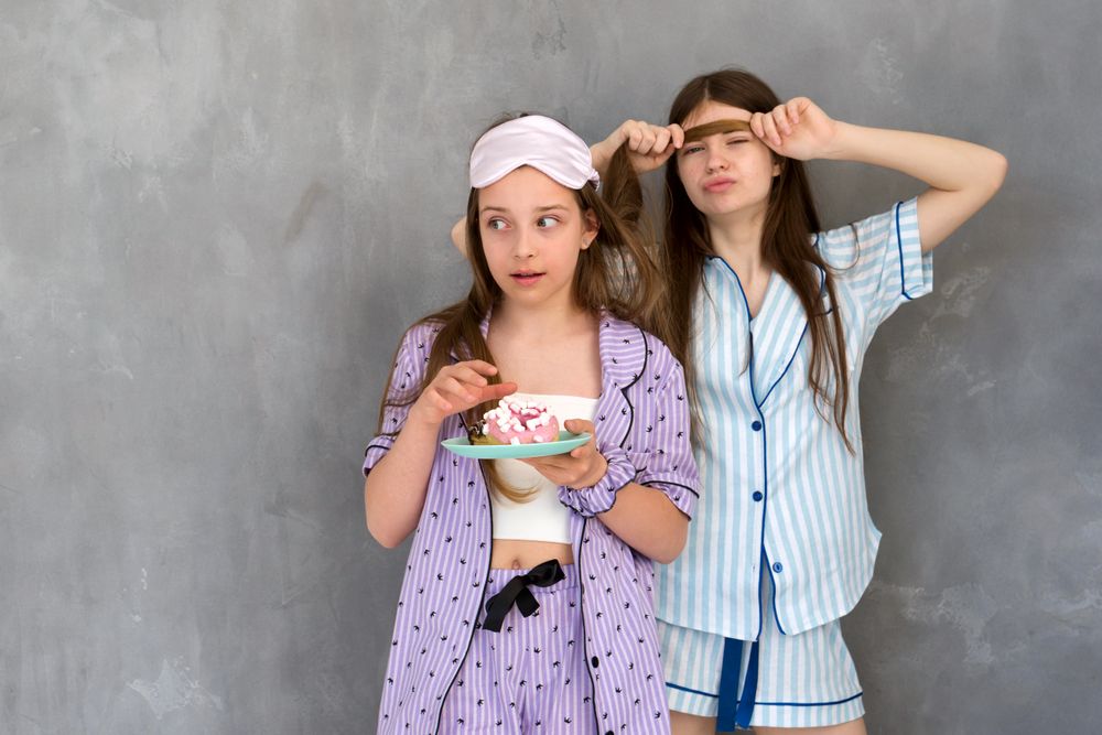 Two girls in pajamas, one eating cake, at a sleepover