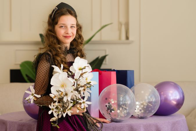 Girl holding flowers and balloons at birthday celebration.