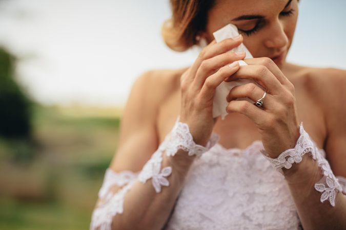 Emotional woman in wedding gown wipes the tears with tissue paper