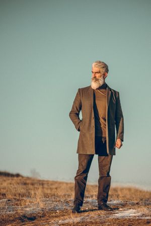 Man in brown coat standing on yellow grassland during golden hour