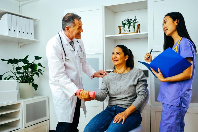 Joking doctor and physiotherapist working with patient during arm rehab exercises