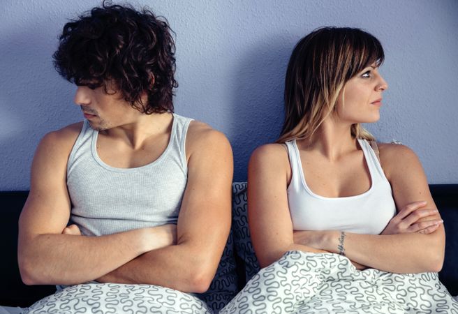 Angry couple sitting on bed with crossed arms