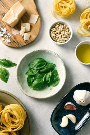 Basil leaves and ingredients for pesto sauce on plates on table
