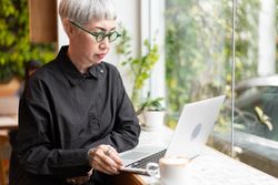 Mature Asian woman watching and working on laptop at the coffee shop