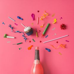 Champagne bottle with colorful party items on pink background
