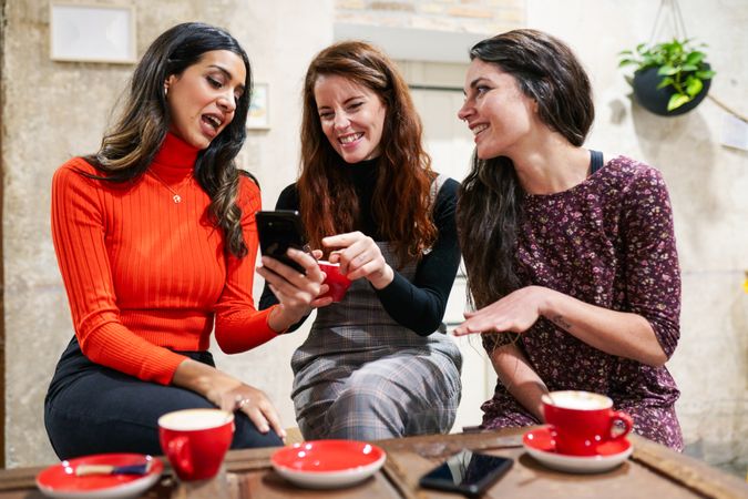 Female friends smiling at something on a friend’s smartphone