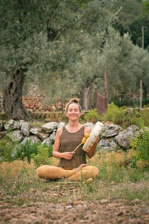 Smiling woman playing tambourine and doing yoga in Lotus pose