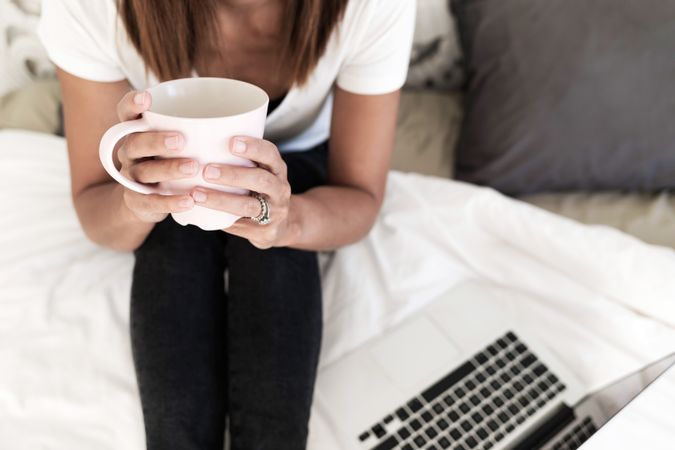 Cropped photo of woman on bed with coffee and laptop
