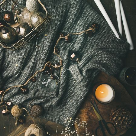 Candle, tea, scissors, and festive decorations in a wire box arranged around a woolen sweater