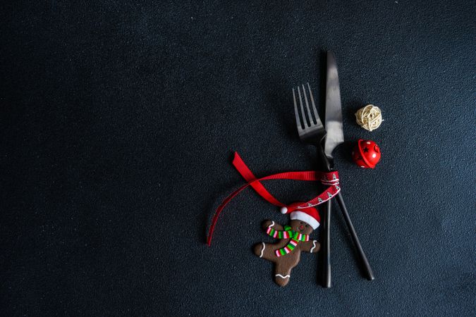Dark knife and fork on dark background tied with bright red ribbon and gingerbread decoration