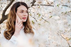 Woman answering phone call near blooming trees