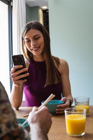 Smiling woman eating tasty food and browsing smartphone