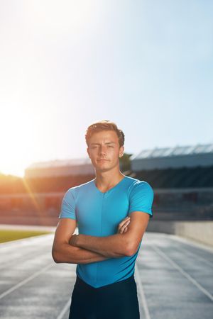 Young male track athlete standing with his arms crossed looking at camera