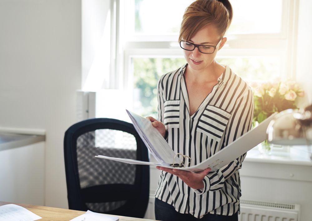 Female in striped shirt looking through binder in her home office