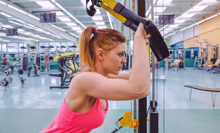 Side view of woman working out upper body with ropes in gym