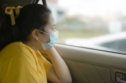 A woman wearing a mask sits and looks out of the car.