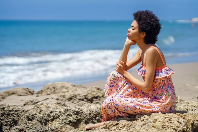 Woman sitting on the rocks on the coast facing the ocean view with eyes closed