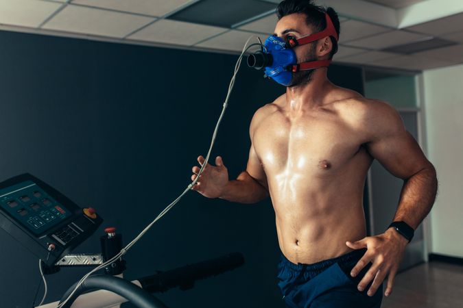 Fit and muscular athlete with mask running on treadmill for monitoring his performance