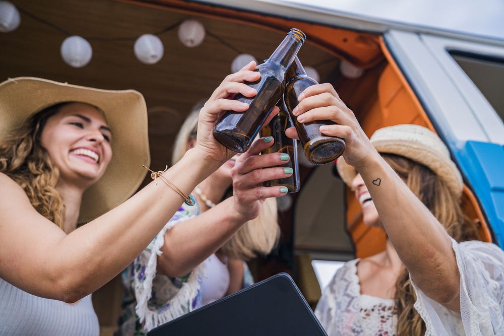 Smiling friends clinking bottles of beer celebrating vacation