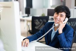 Smiling Asian male in suit on satisfying phone call at work bxodd4