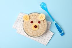 Bear face made of porridge and fruits on blue background, top view. Baby food