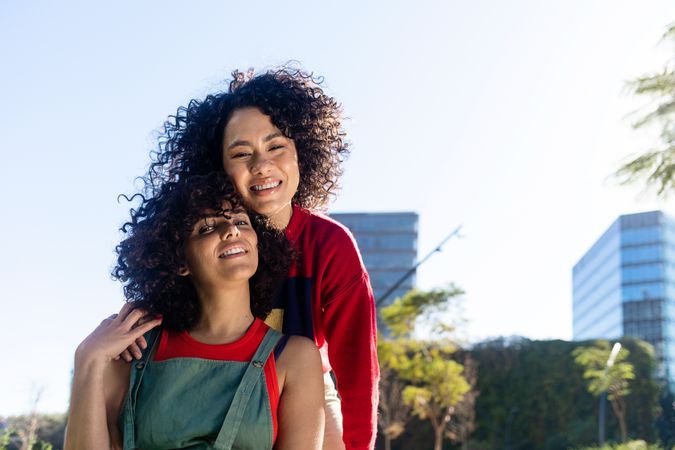 Two female friends with curly hair standing in city park together
