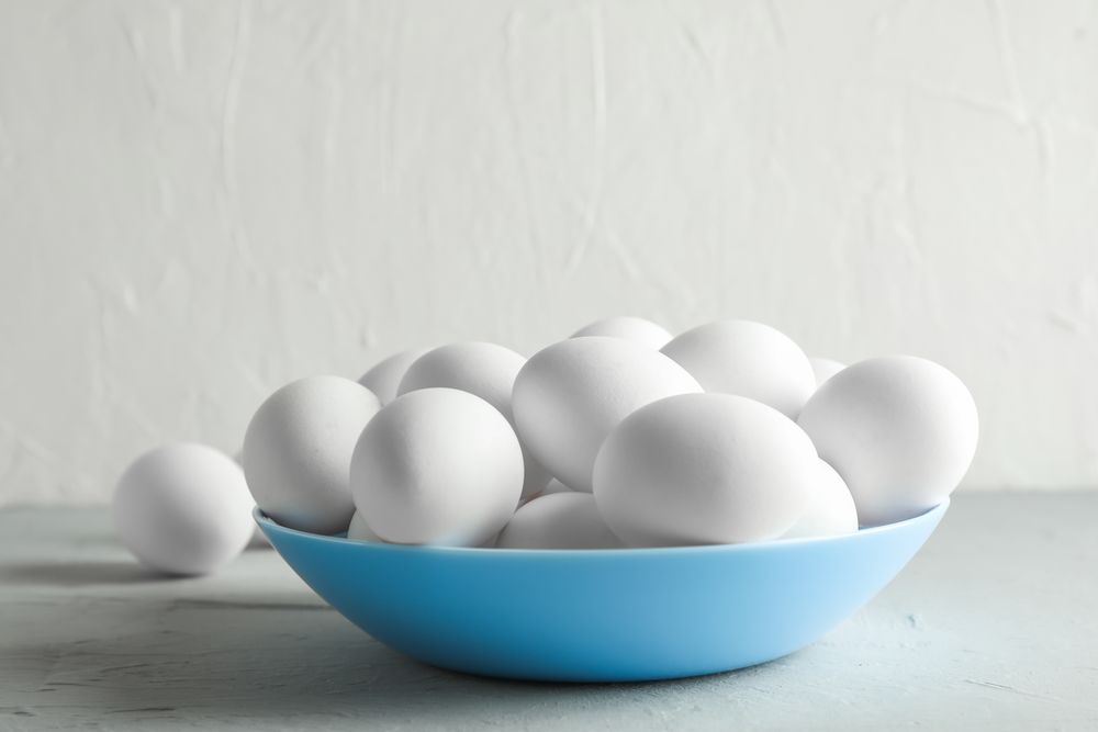 Chicken eggs in plate on gray table against light background, space for text