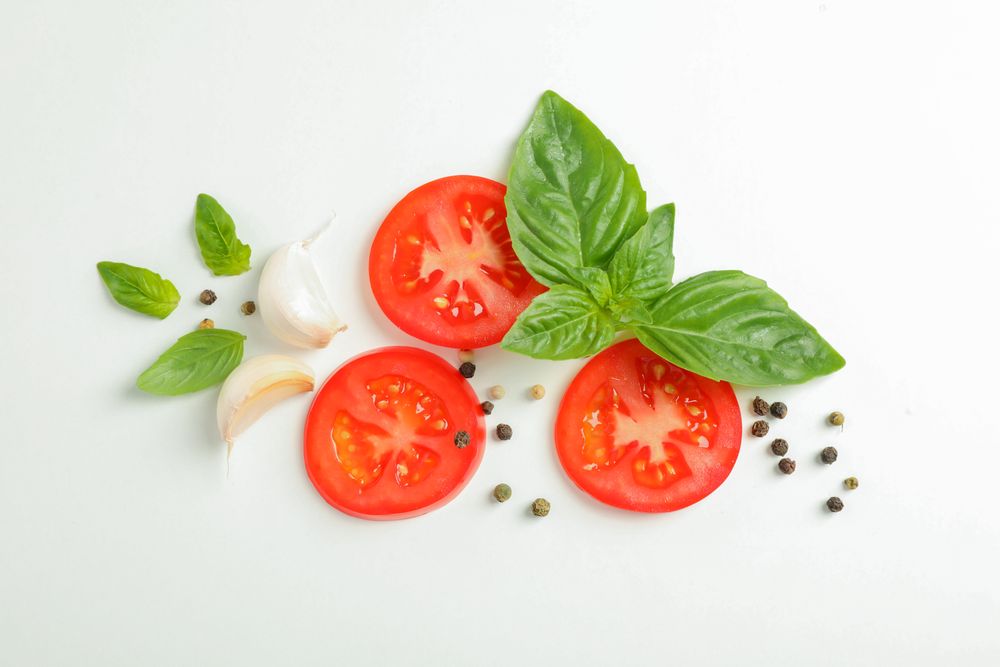 Flat lay composition with fresh cherry tomatoes slices with basil, pepper and garlic on blank background, space for text and top view. Ripe vegetables