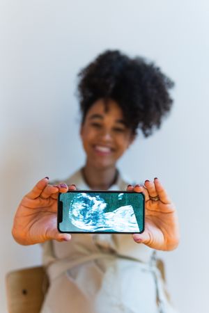 Smiling Black woman showing smartphone screen with baby ultrasound