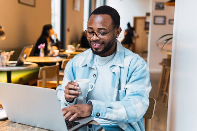 Delighted Black man with coffee browsing laptop