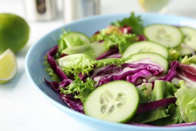 Plate with fresh salad, spices and oil on wooden background, close up