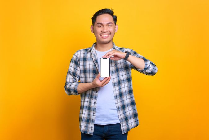Happy Asian male showing blank screen of smart phone with both hands in studio shoot