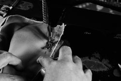 B&W shot of hands putting fabric through sewing machine needle