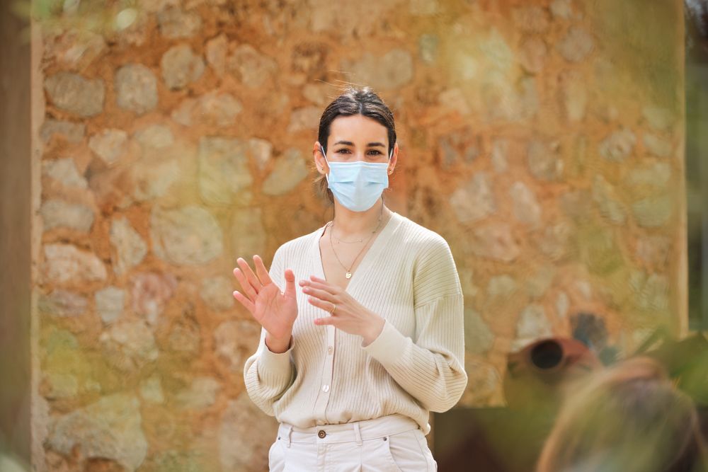 Content woman in mask standing against stone wall in garden