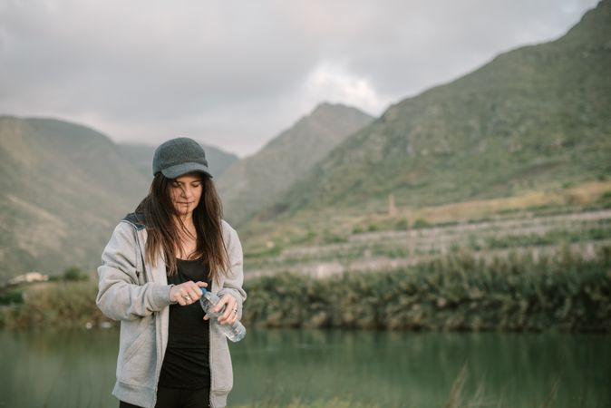Woman drinking water near lake between mountains