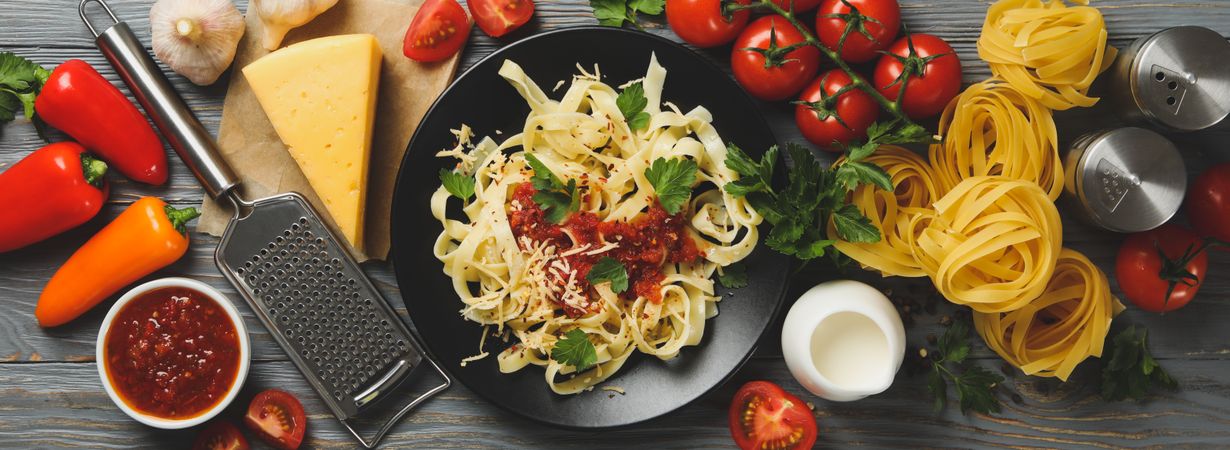 Composition with plate of tasty pasta and ingredients for cooking on wooden background