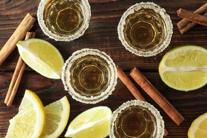 Tequila shots with salt, lime slices and cinnamon on wood table, top view