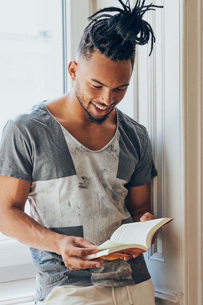 Black male standing by window and reading